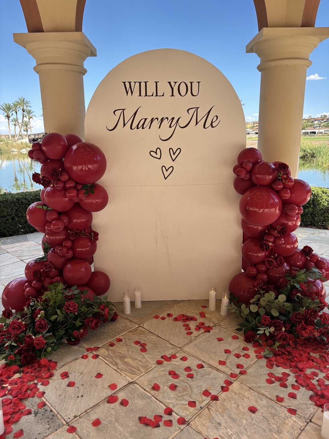 Romantic wedding proposal setup with burgundy balloons, florals, candles, and rose petals